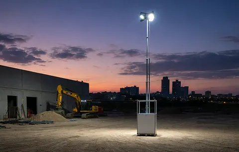 Mobiler Lichtmast beleuchtet in der Dämmerung eine Baustelle