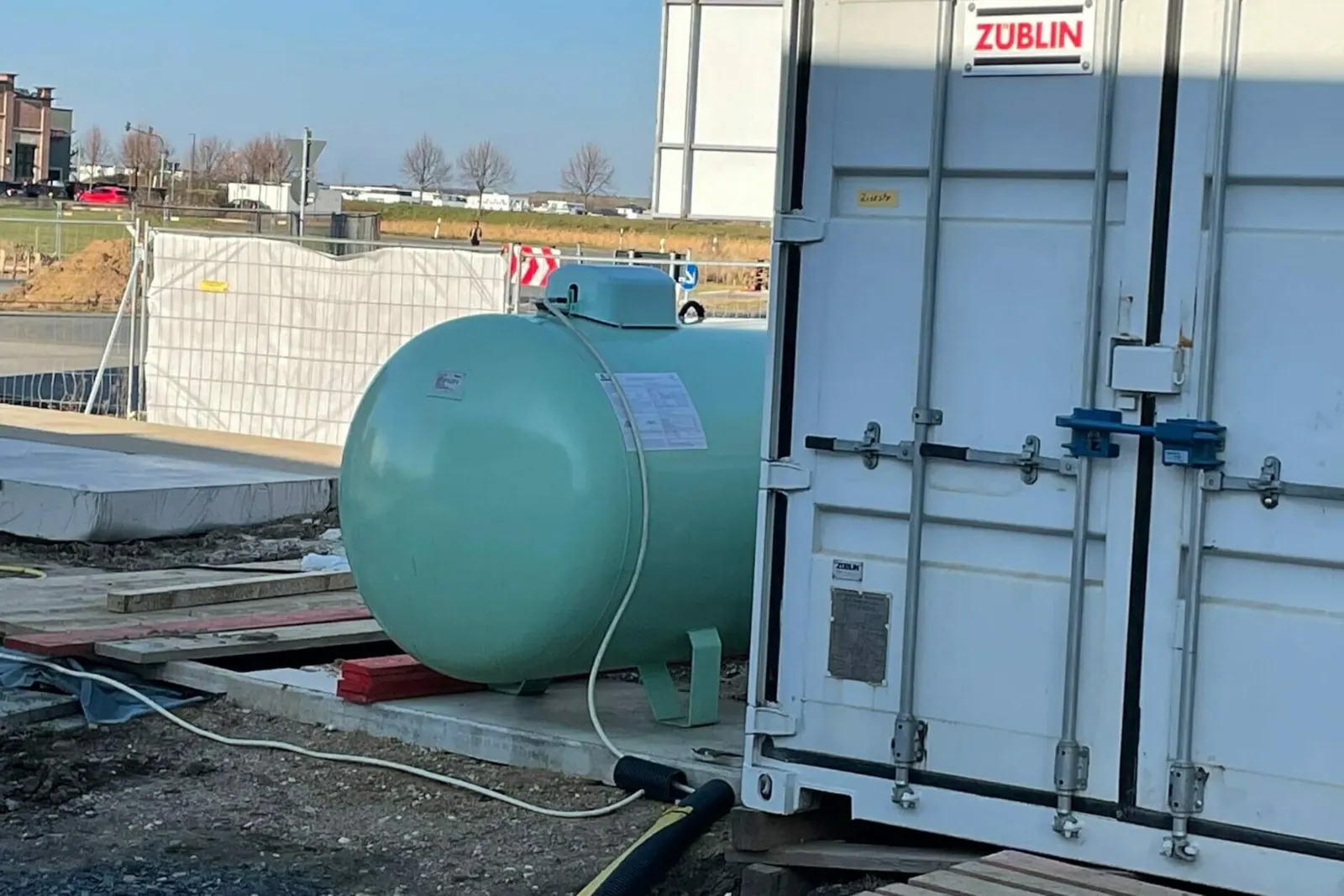 Mobile Heizzentrale im Container auf einer Baustelle, über eine Leitung mit einem Flüssiggastank verbunden