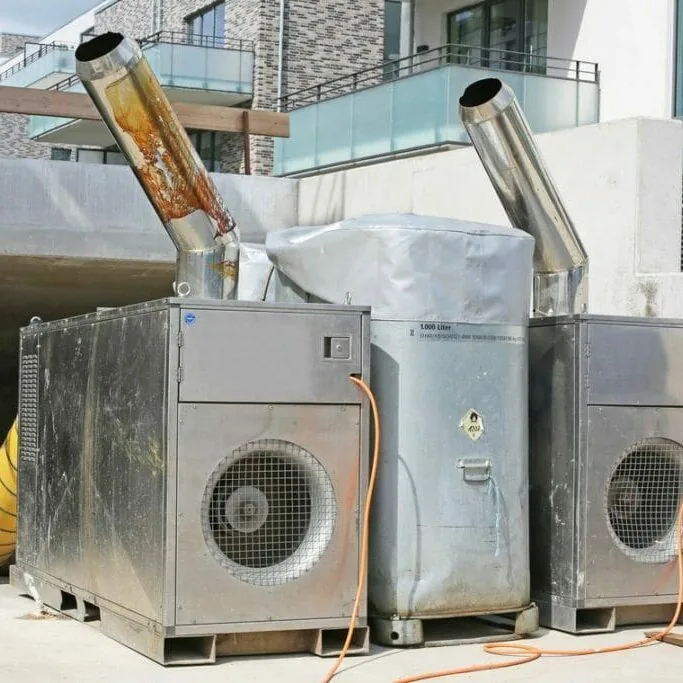 Zwei mobile Warmlufterzeuger mit Abgasrohren und Flüssiggastank vor einem Rohbau